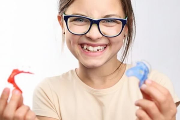Smiling child holding early orthodontic appliances after interceptive treatment with Dr. Nikhil Sharma at Invisible Braces Dental & Skin Clinic, Dubai.