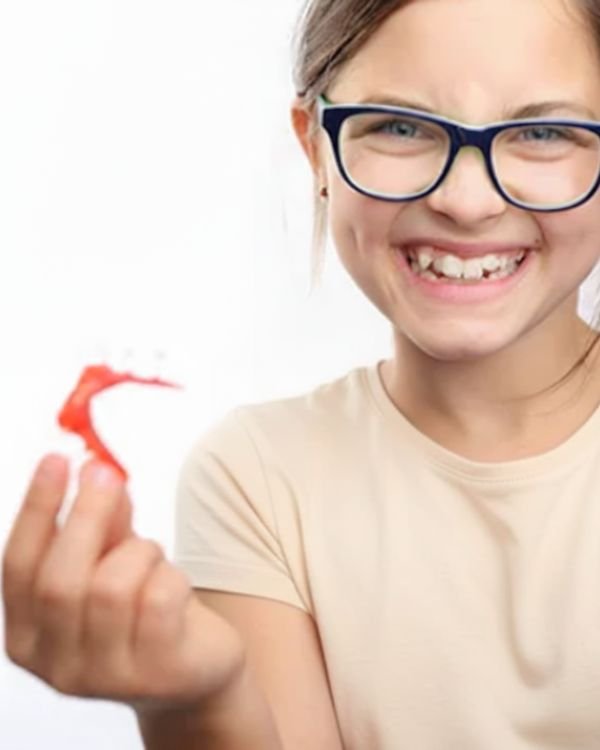 Smiling young girl holding an early orthodontic appliance after interceptive treatment with Dr. Nikhil Sharma at Invisible Braces Dental & Skin Clinic, Dubai.