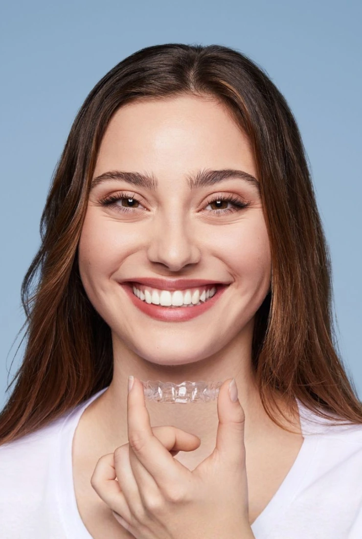 Smiling woman holding a clear Invisalign aligner in front of her teeth, demonstrating the comfort and transparency of aligners offered at Invisible Braces Dental & Skin Clinic Dubai under Dr. Nikhil Sharma. The face is shown but not identified.
