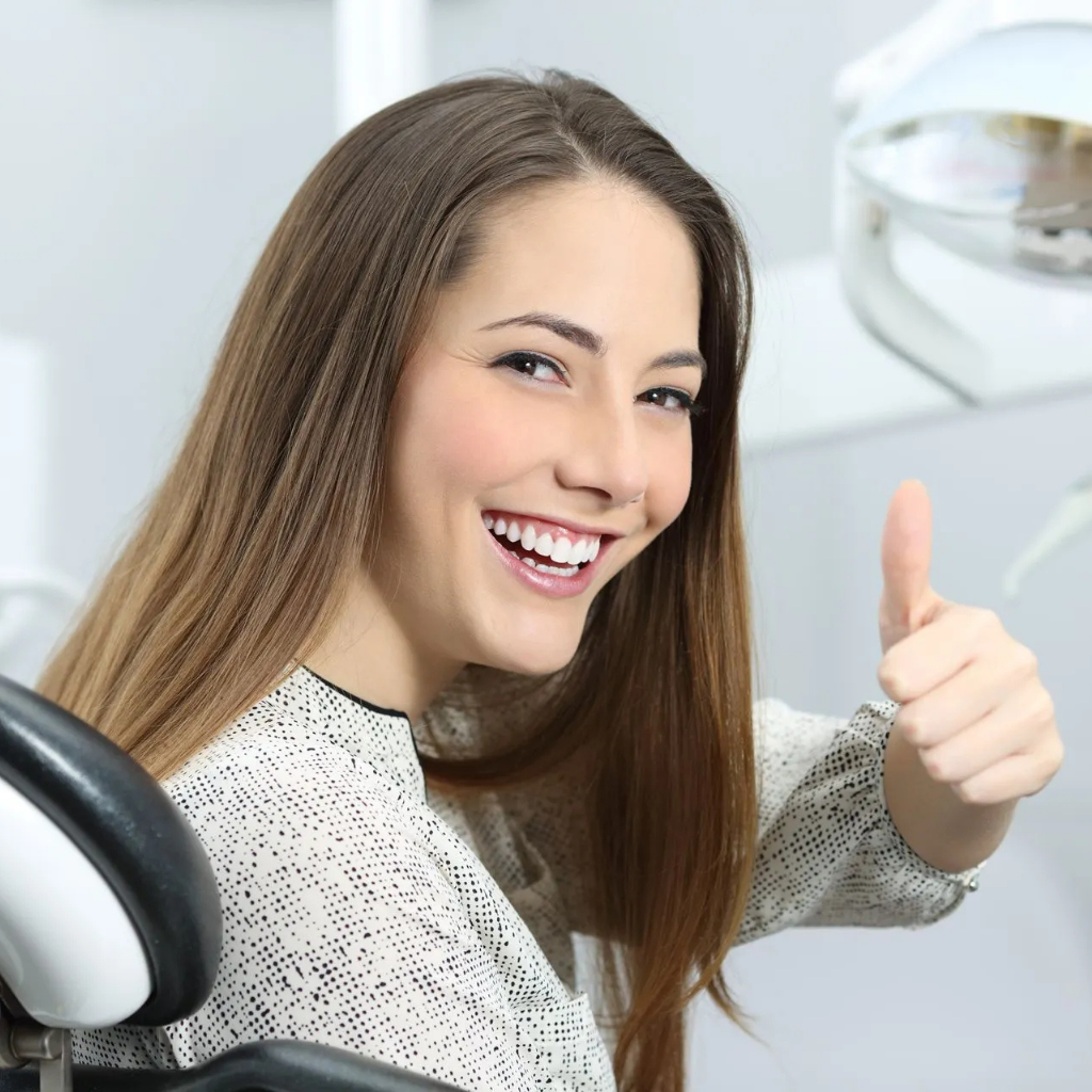 Woman smiling and showing thumbs up after a professional teeth cleaning session at Invisible Braces Dental & Skin Clinic.