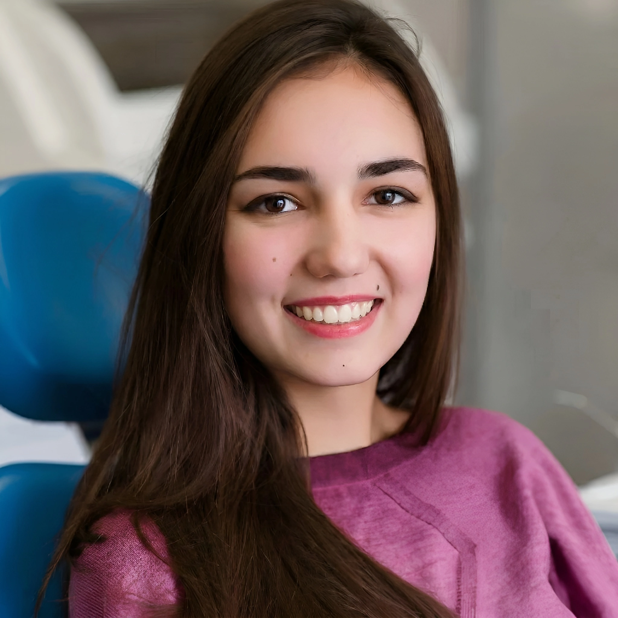 Young woman smiling after lingual braces orthodontic treatment while sitting in a dental chair.